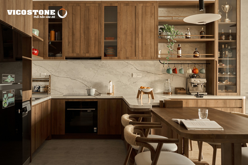 Tường và bàn bếp ốp đá VICOSTONE Covelani BQ6700 vân xám - vàng phóng khoáng trên nền trắng tạo nên sự tương phản sống động với hệ tủ gỗ, biến không gian bếp chữ U tại Golden Mansion (TP.HCM) thành điểm hội tụ của vẻ đẹp hiện đại và hơi thở tự nhiên (Nguồn: Căn hộ Golden Mansion (Phổ Quang, TP. HCM) do MEI Home thiết kế và thi công nội thất).