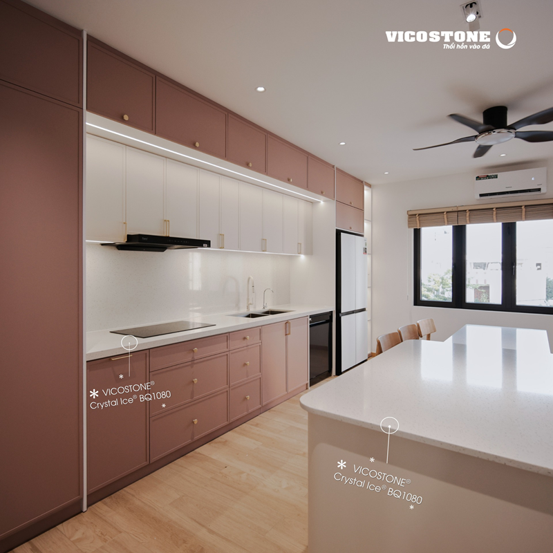 Mặt bếp, tường bếp và bàn đảo ốp đá VICOSTONE Crystal Ice BQ1080 hiệu ứng chiều sâu trong suốt từ các hạt thạch anh kích thước lớn tạo nên điểm sáng tinh tế, hòa quyện hoàn hảo cùng tông hồng đất dịu dàng trong căn bếp hiện đại mang hơi thở thư thái giữa lòng Đà Nẵng (Nguồn: Căn bếp do Simie Home thiết kế).