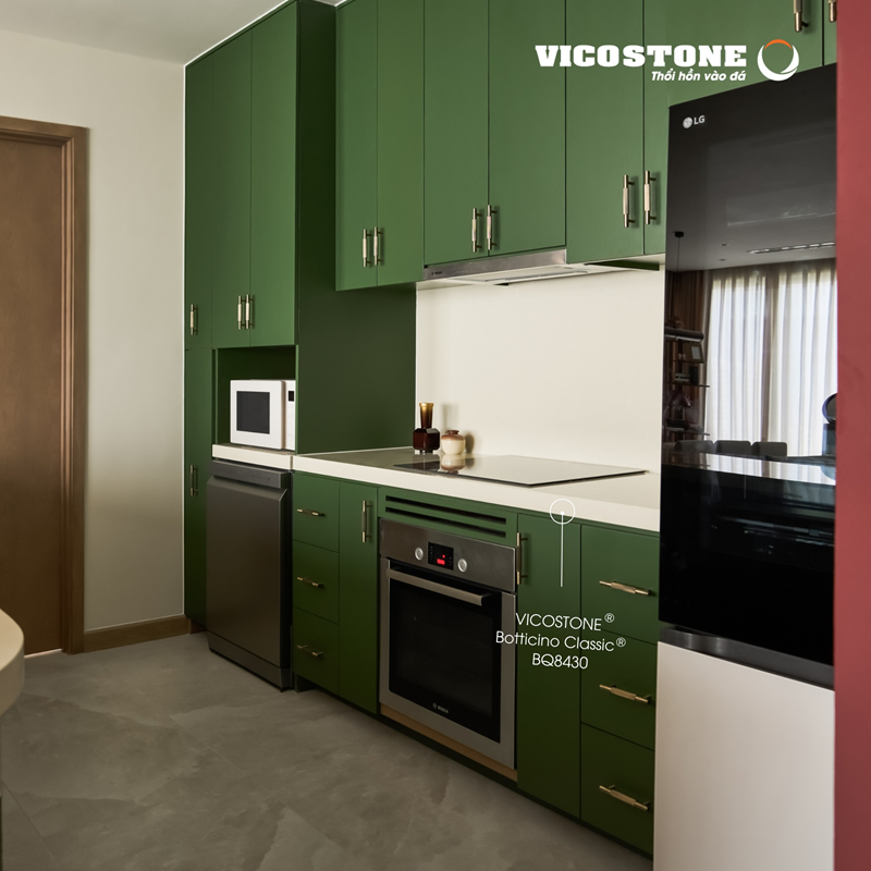 Mặt bếp ốp đá VICOSTONE Botticino Classic BQ8430 sắc ngà thanh lịch với vân trắng nhẹ nhàng tạo điểm cân bằng tinh tế giữa hệ tủ xanh lá cá tính (Nguồn: Căn bếp do Ltd. Studio thiết kế).